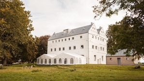 A large, white, multi-story building with a symmetrical facade, surrounded by a grassy area and trees. - Gutshaus Üselitz (Poseritz)