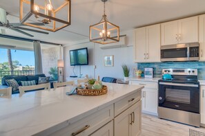 A modern kitchen with white cabinetry, a large island, stainless steel appliances, and a flat-screen TV.