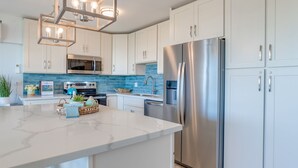 Een moderne keuken met witte kasten, een roestvrijstalen koelkast, een inbouwmagnetron en een marmeren aanrecht.