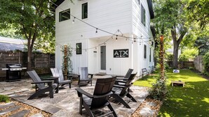 A patio with Adirondack chairs, a stone pathway, and a white house with a sign reading "ATX Austin Texas".