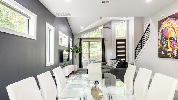 A modern living room with a glass dining table, white chairs, a grey sofa, and a staircase leading to another level.