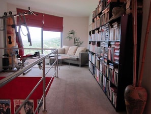 Quarto com área de ginástica, estante de livros, sofá e vista para o exterior.
