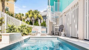 A swimming pool with a white fence, lounge chairs, and a water feature. - Big Wave | Private Pool Optional Heat, Hot Tub (Tybee Island)