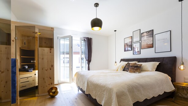Ein Schlafzimmer mit einem großen Bett, einem Holzschrank und einer Schiebetür zum Balkon.
