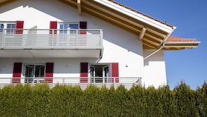 Ein zweistöckiges Gebäude mit Balkon, roten Fensterläden und einer weißen Fassade.