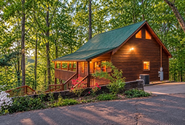 A wooden cabin with a porch, surrounded by trees.