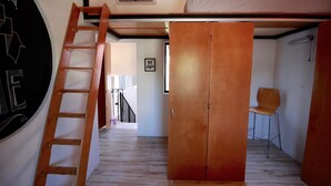 Quarto compacto com beliche, escada de madeira, uma cadeira e uma porta.