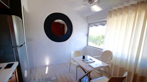 Quarto compacto com mesa de jantar, cadeiras, espelho e janela com cortinas.