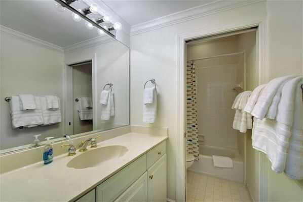 A bathroom with a large mirror, a sink with two faucets, and a shower area with a curtain. - SEAesta Beach House in St Simons Island, GA (St Simons Island)