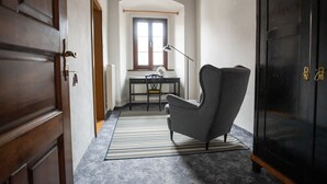 A hallway with a wooden door, a grey armchair, a black cabinet, and a desk with a lamp. - Hostel Javni Zavod Mekinjski Samostan (Kamnik)