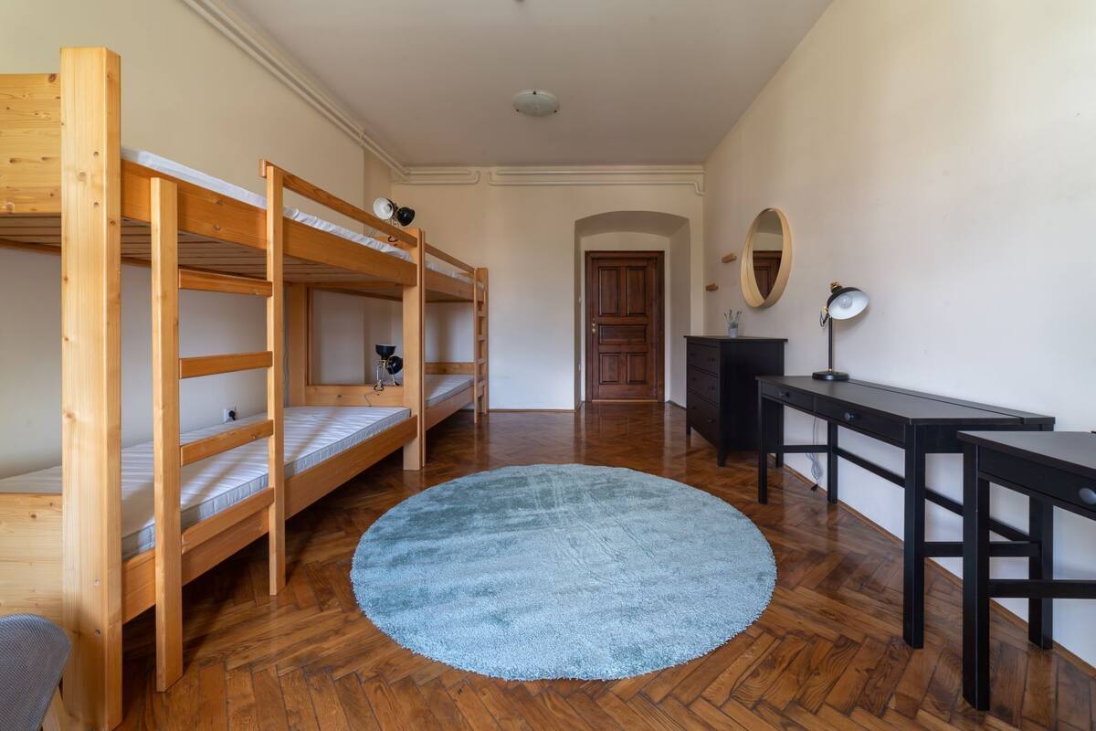 A room with bunk beds, a desk, a chair, a round rug, and a mirror on the wall.