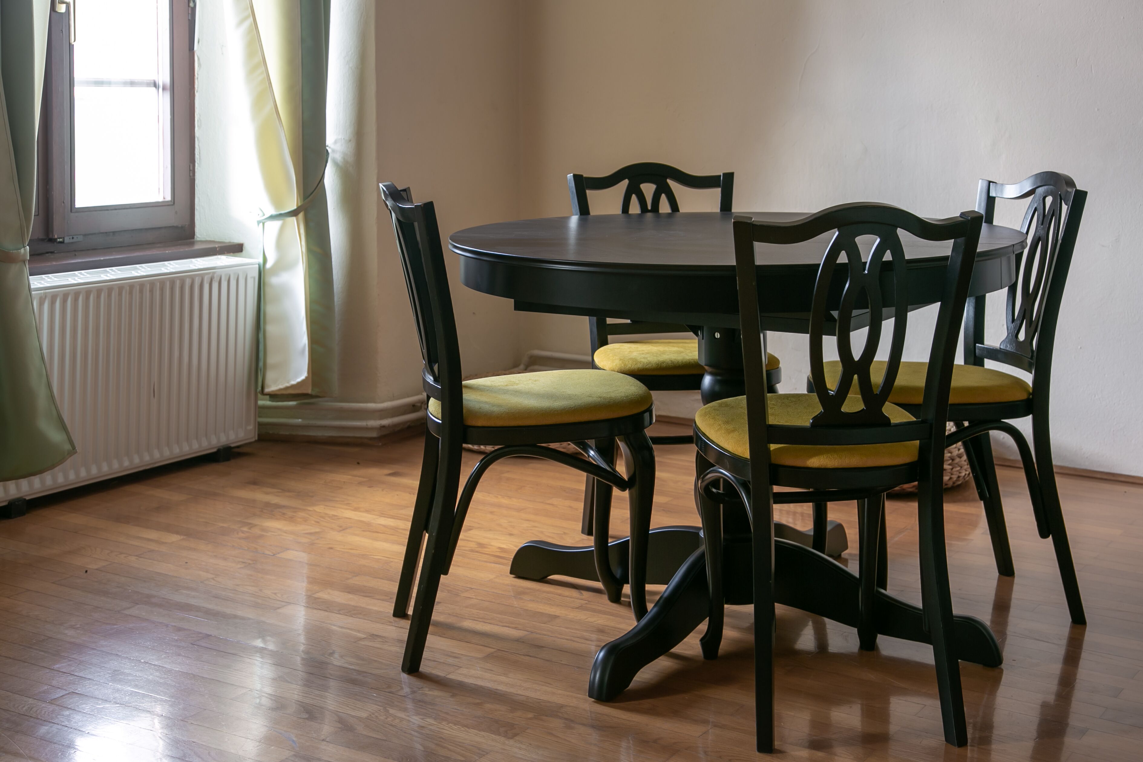 Un comedor con una mesa redonda y cuatro sillas, un radiador y una ventana con cortinas.
