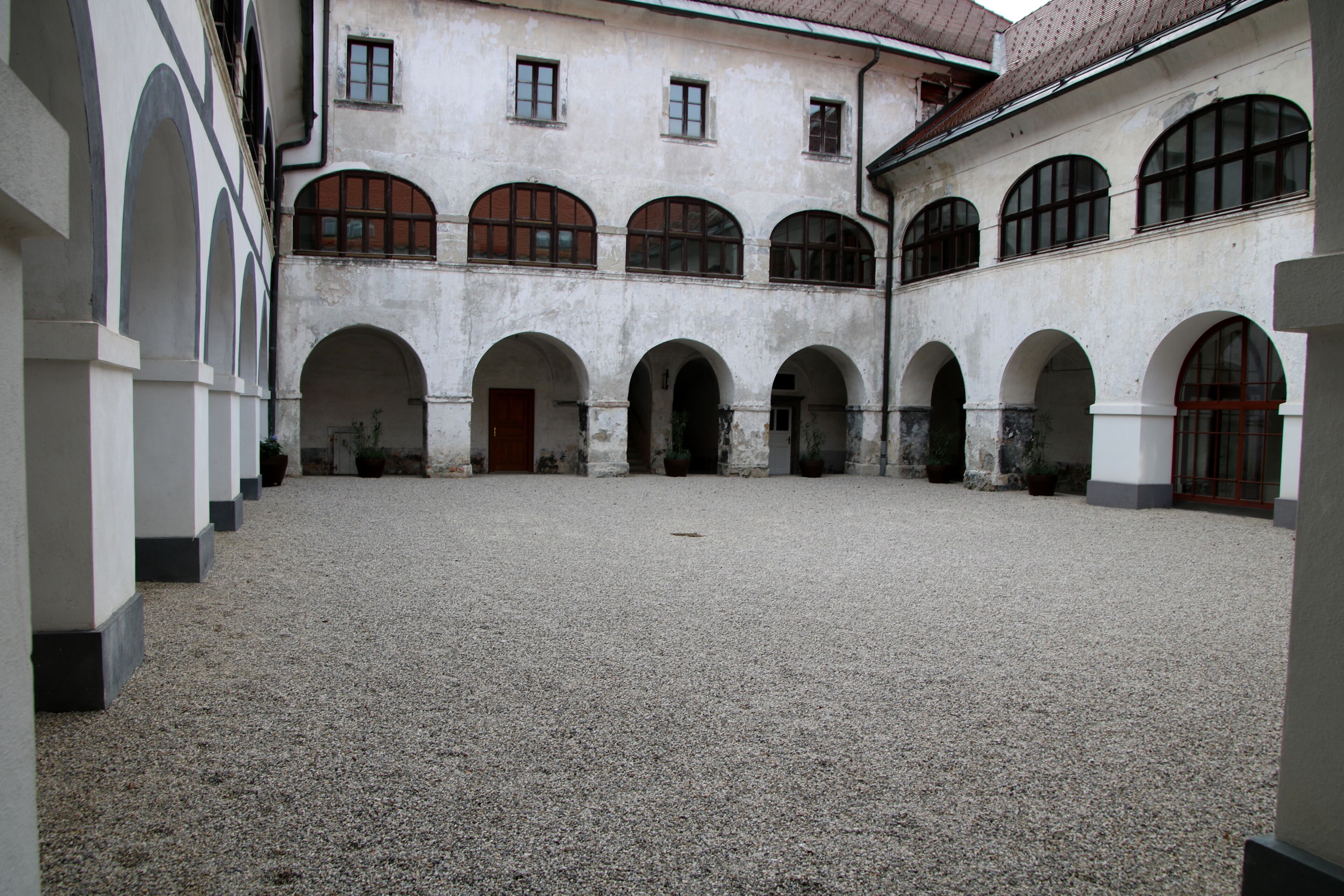 A courtyard with a gravel floor, surrounded by white walls with arched doorways and windows.