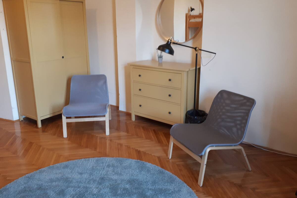 A room with a wardrobe, two chairs, a dresser, a mirror, and a lamp.