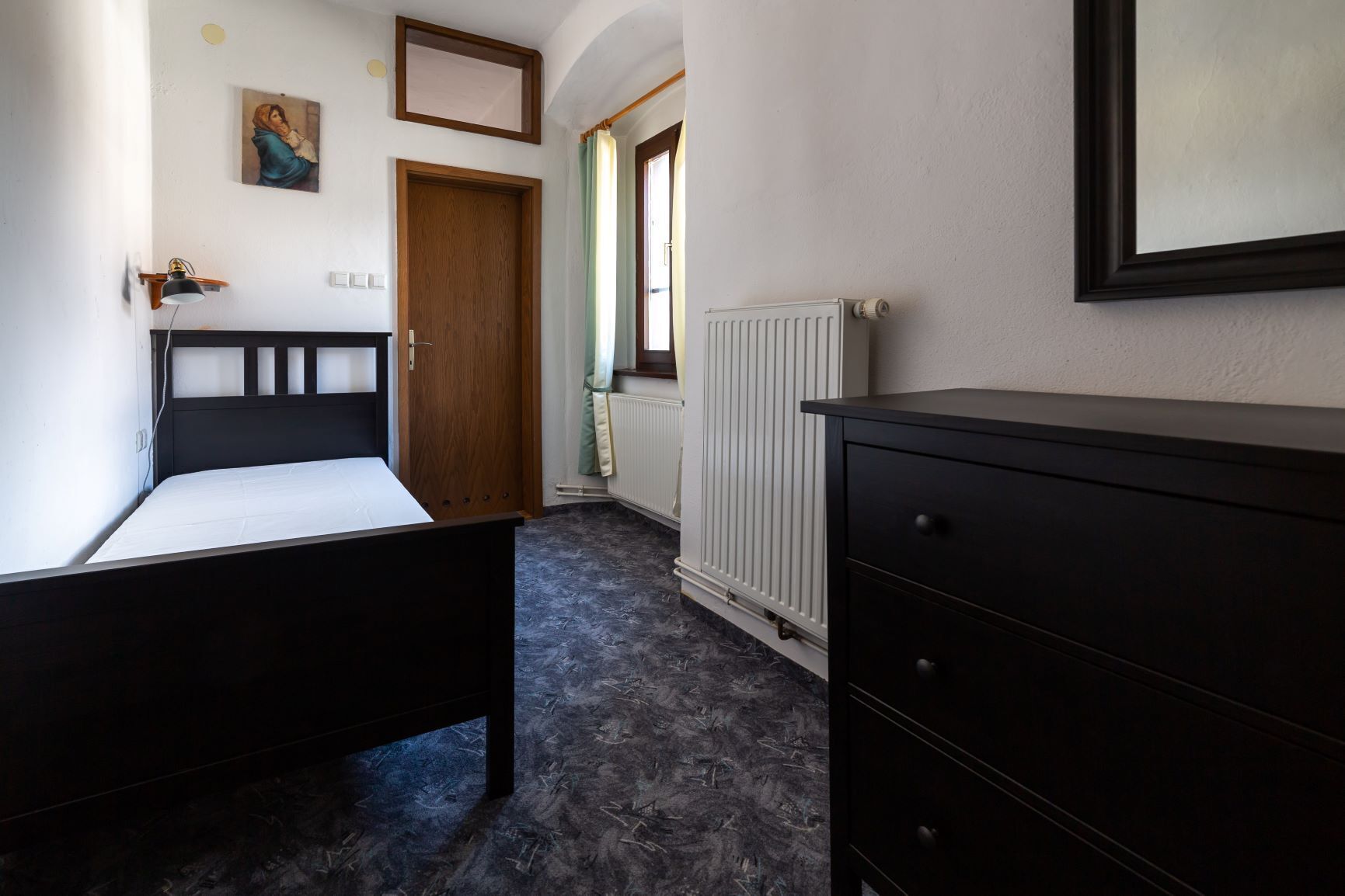 A bedroom with two single beds, a wooden wardrobe, a radiator, and a door leading to another room.