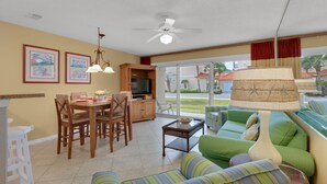 A spacious living area with a dining table, chairs, a sofa, a TV, and a ceiling fan.