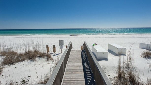 A wooden boardwalk leading to a beach with white sand and clear blue water.