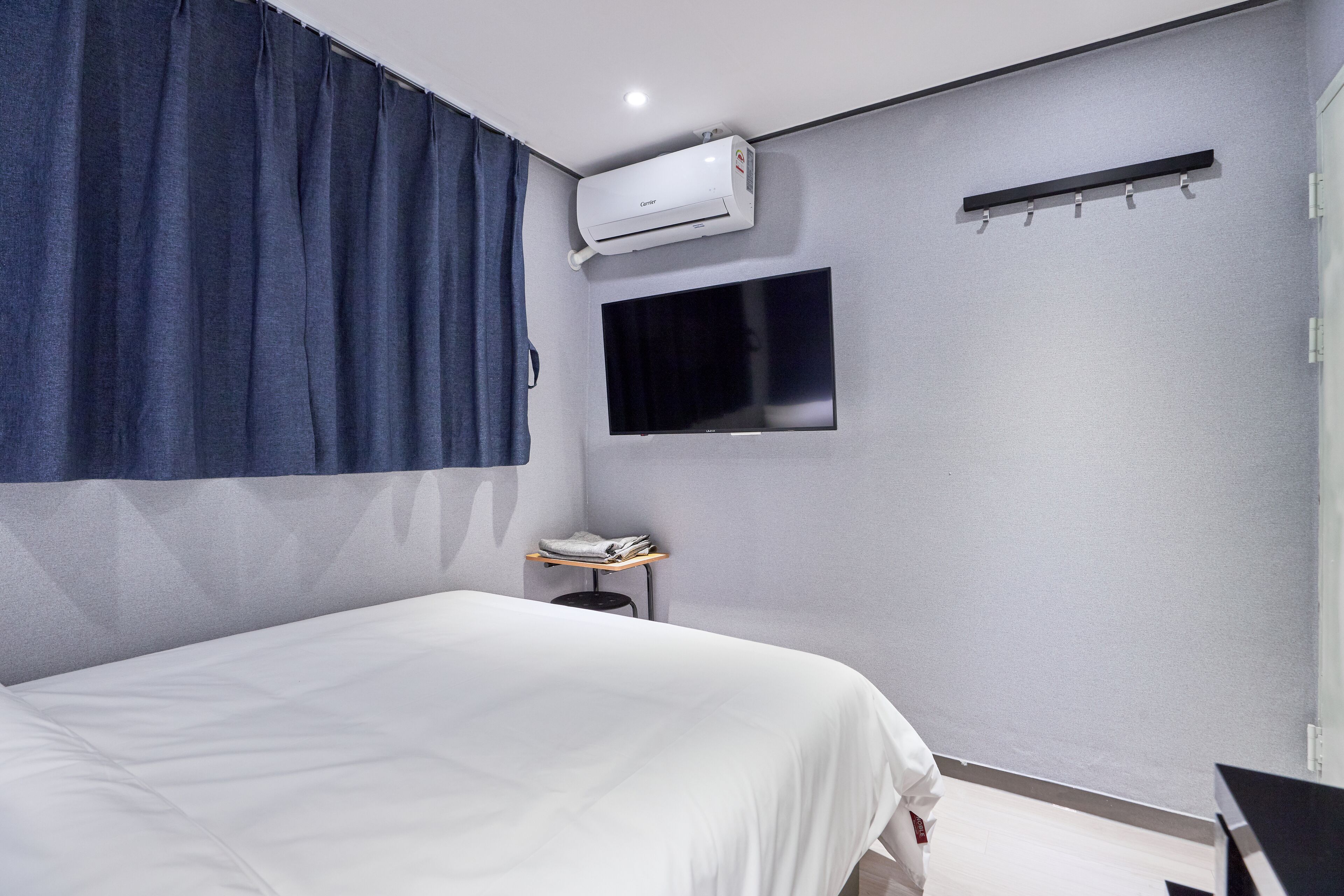 Una habitación de hotel moderna con una cama, un televisor de pantalla plana montado en la pared, una mesita con una toalla y un equipo de aire acondicionado.