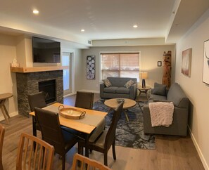 A living room with a fireplace, a television, a sofa, a coffee table, and a dining area with chairs and a table.