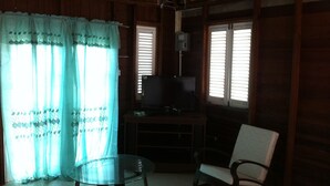 A room with wooden walls, a glass table, two chairs, a television on a stand, and a window with blinds. - A spacious rustic house with modern conveniences (St. James)