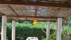Un espacio de estar al aire libre cubierto, con una mesa de piedra y bancos, rodeado de follaje.