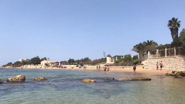 Una playa con agua cristalina, rocas y gente.