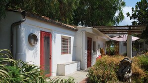 Un edificio blanco con puertas y ventanas rojas, rodeado de vegetación y un sendero de piedra.