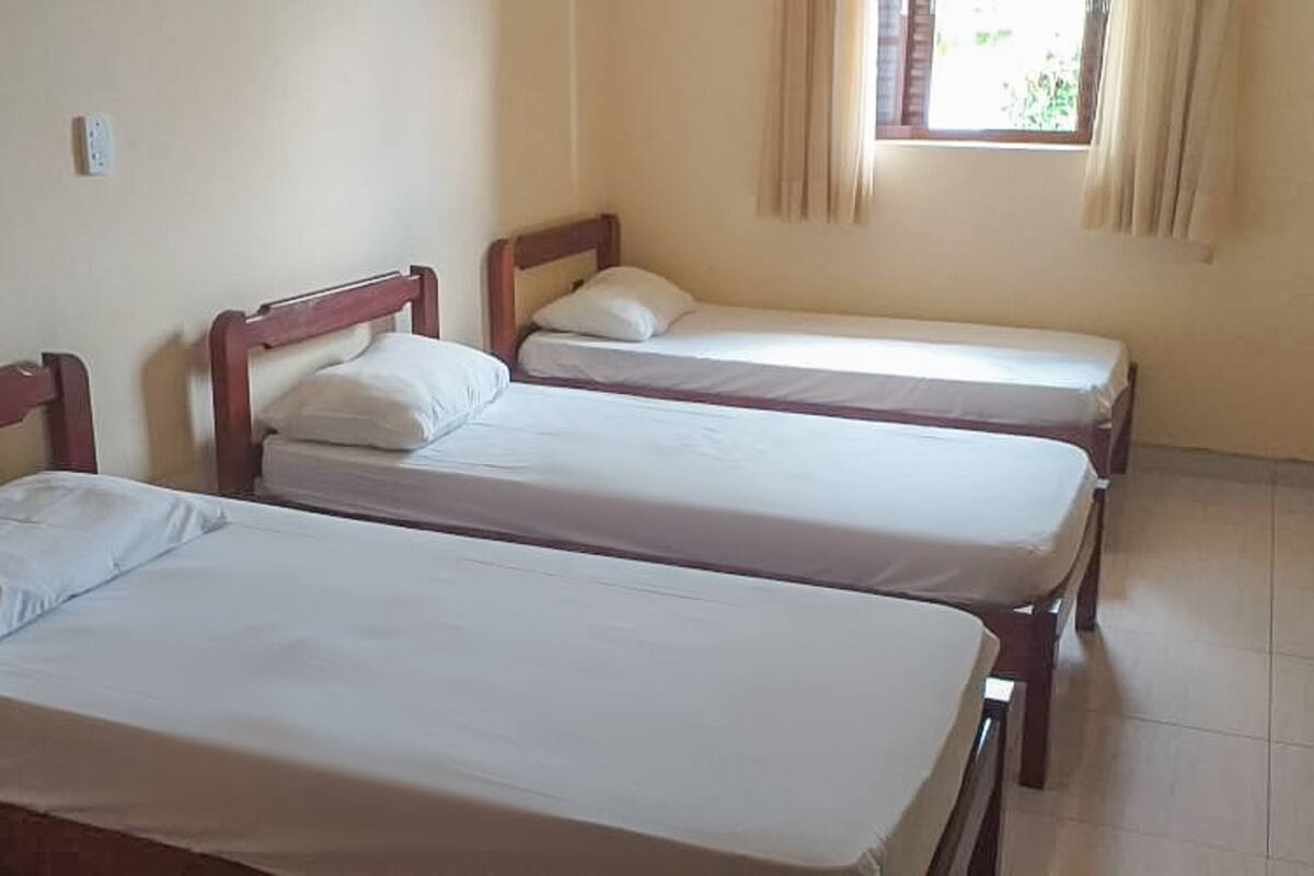 Ein Zimmer mit drei Einzelbetten, einem Vorhangfenster und einem Fliesenboden.