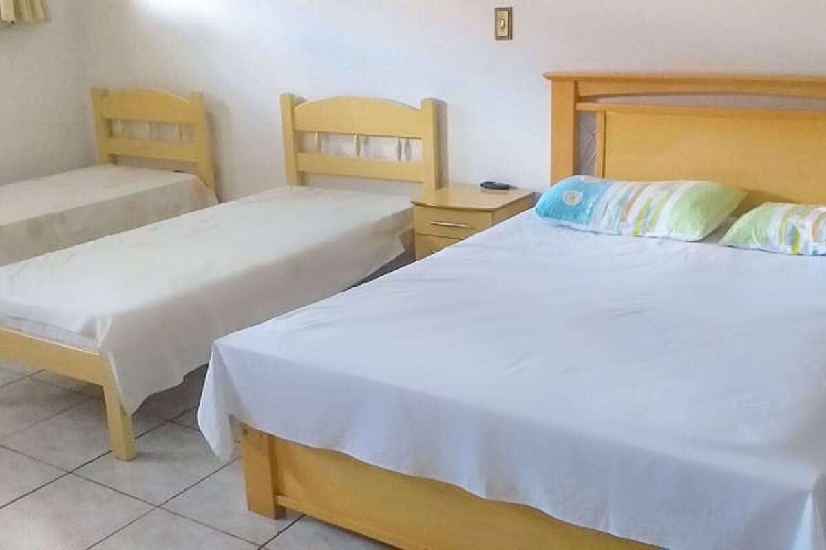 Ein Zimmer mit zwei Einzelbetten und einem größeren Bett mit einem hölzernen Kopfteil.