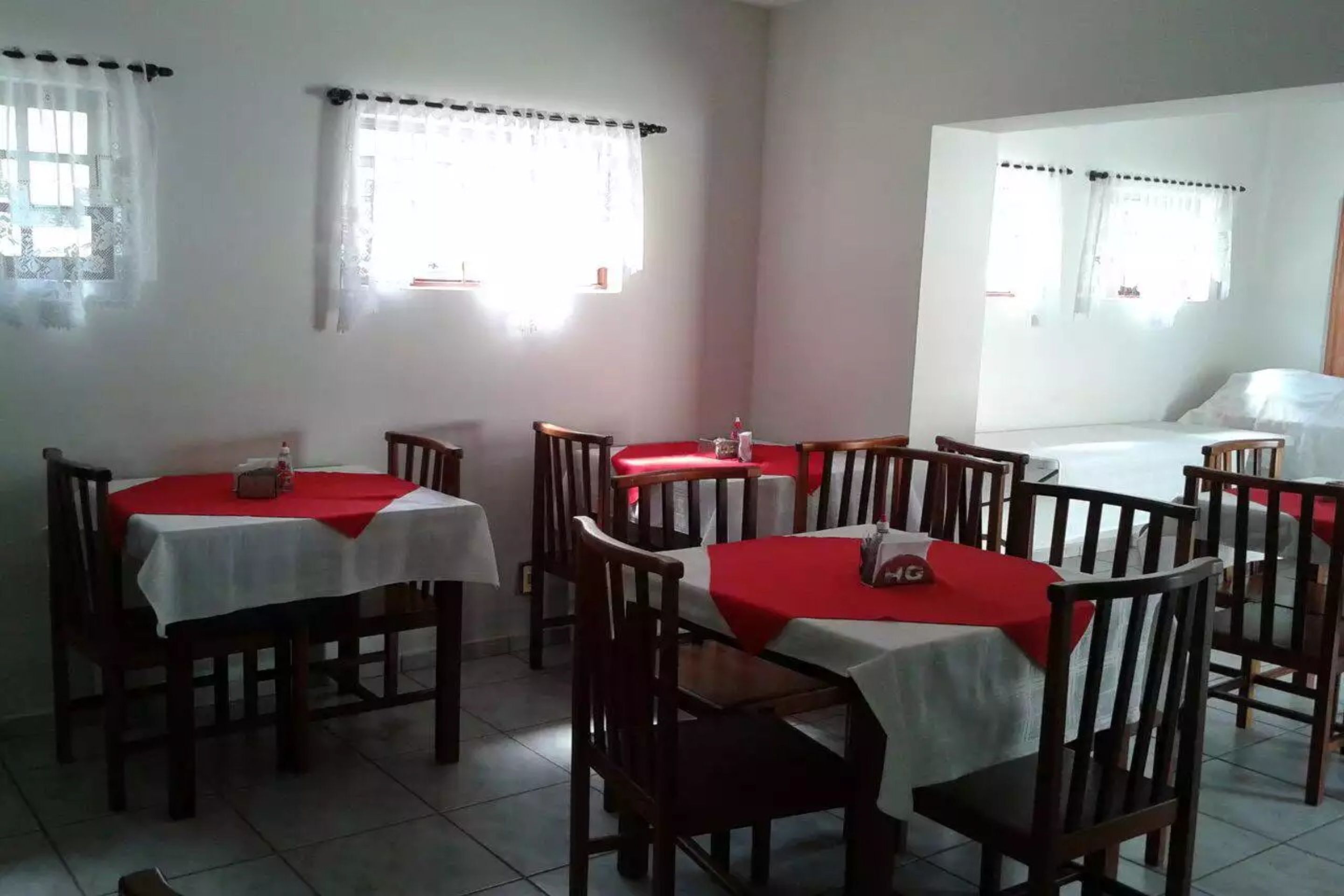 A dining area with multiple tables and chairs, some with red tablecloths.