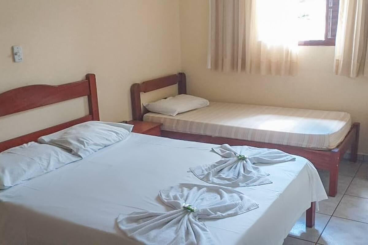 Ein Zimmer mit zwei Betten, eines größer und eines kleiner, beide mit weißer Bettwäsche. Handtücher liegen auf dem größeren Bett drapiert.