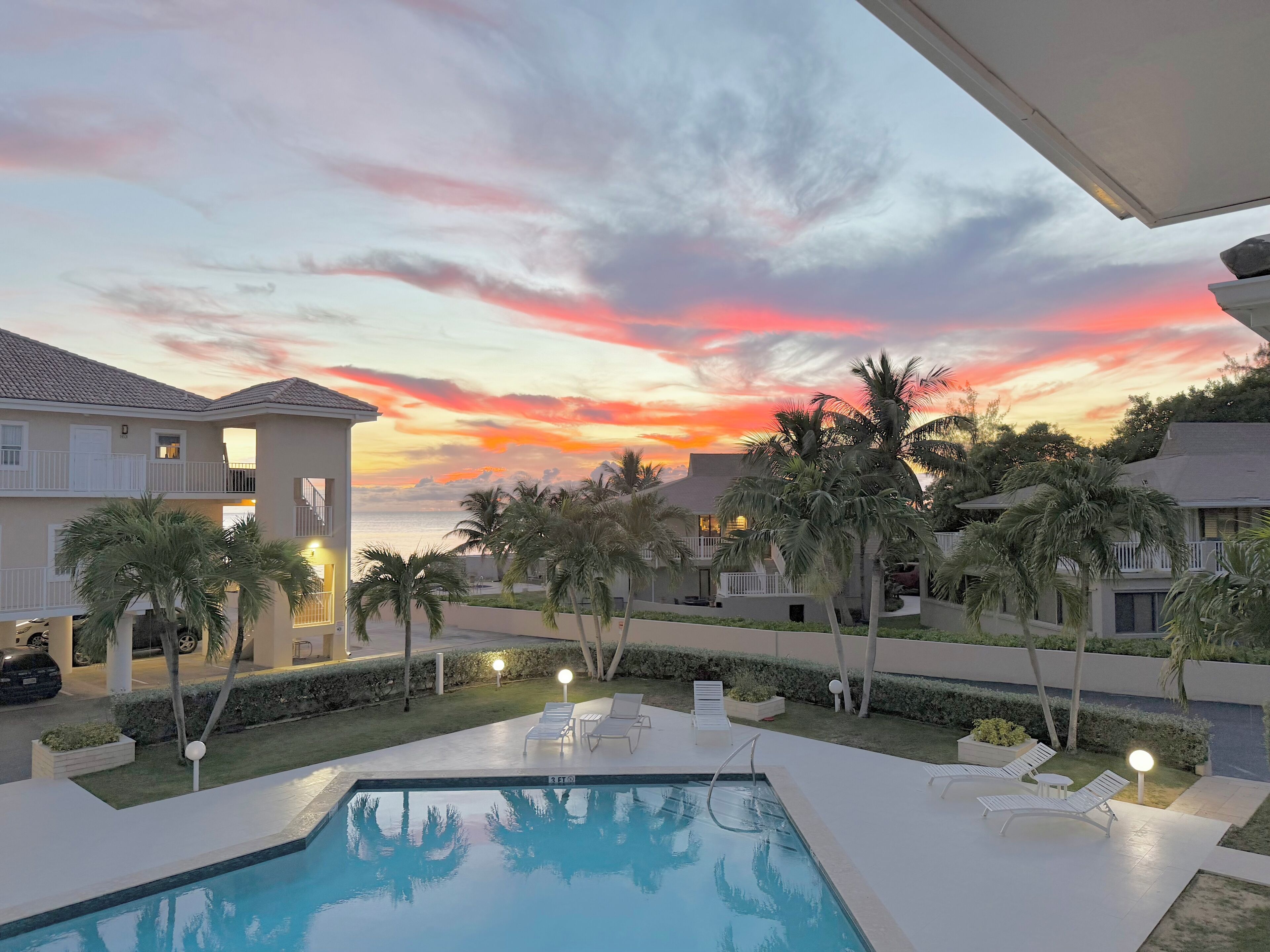 A swimming pool with lounge chairs and a sunset view.