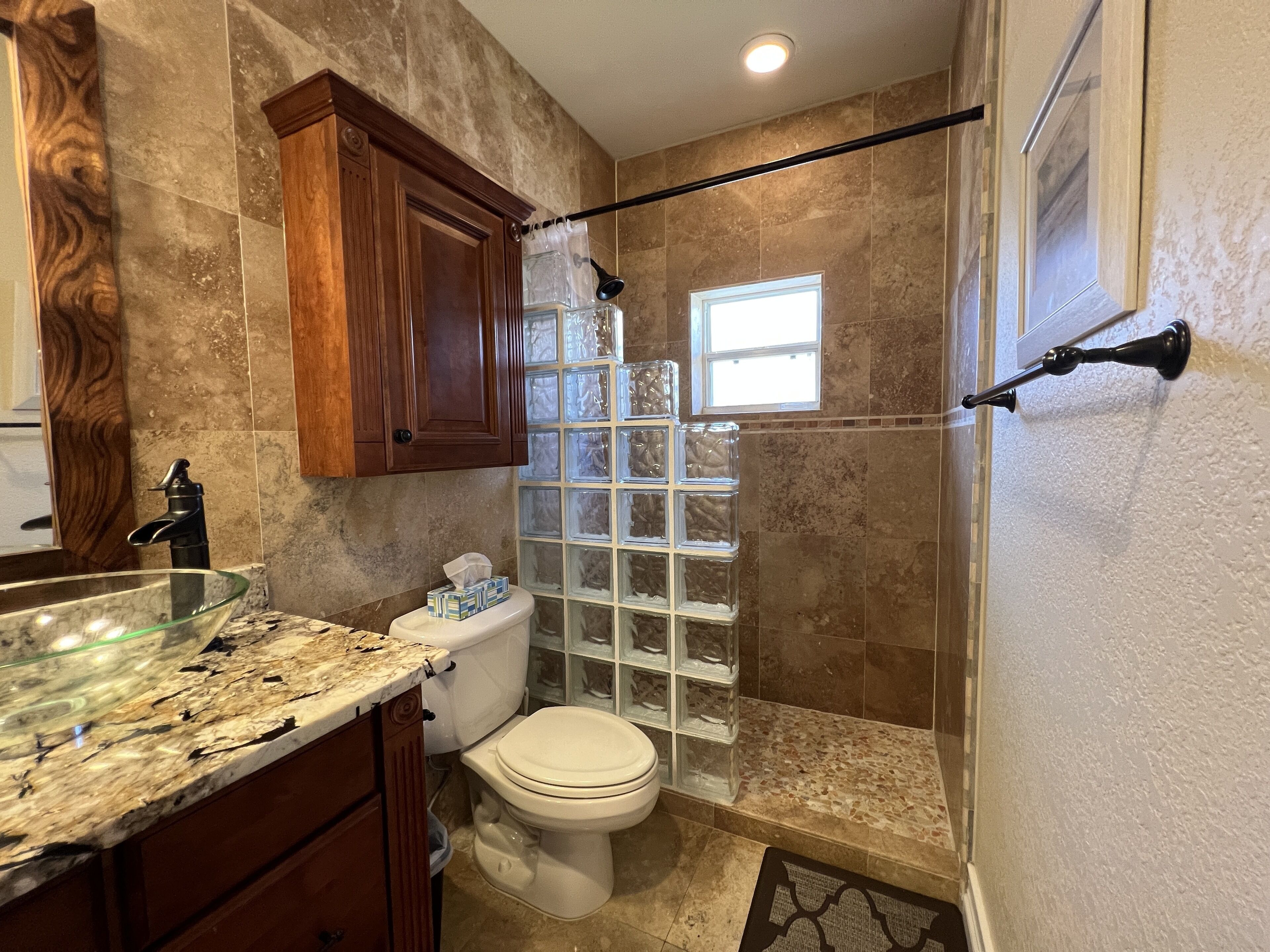 Une salle de bain dotée d’une douche à parois de verre, d’un comptoir en marbre et d’un meuble-lavabo en bois.