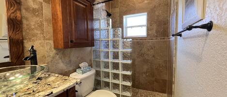 Une salle de bain dotée d’une douche à parois de verre, d’un comptoir en marbre et d’un meuble-lavabo en bois.