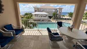 A balcony with a pool view, wicker furniture, and a ceiling fan. - Oceanfront Luxury in small Intimate complex! (West Bay)