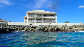A multi-story hotel with balconies, situated by a rocky coastline with clear blue waters. - Oceanfront Luxury in small Intimate complex! (West Bay)