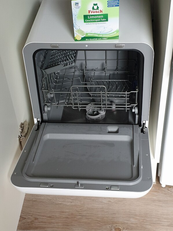 An open dishwasher with a box of Frosch dishwashing liquid above it.
