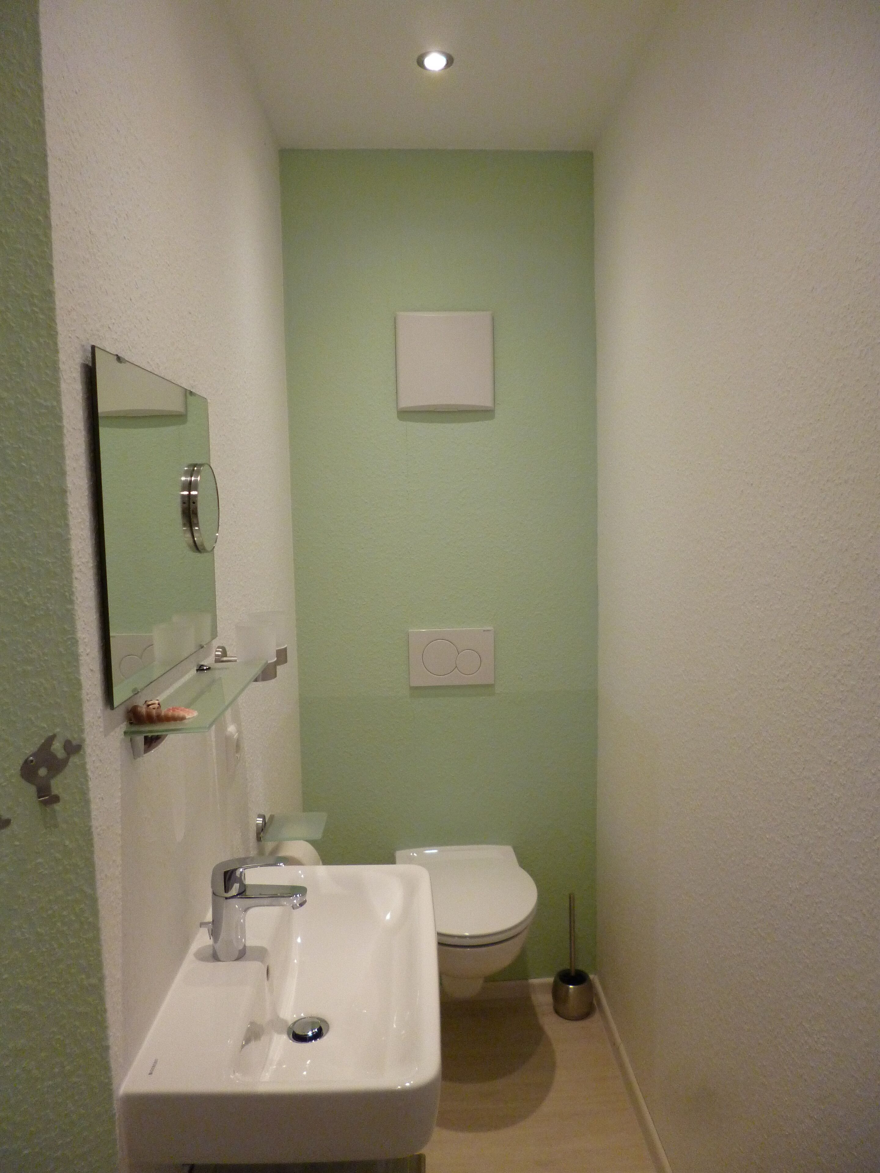 A bathroom with a white sink, a mirror, a toilet, and a light switch on the wall.