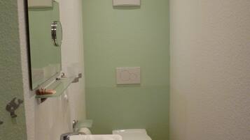 A bathroom with a white sink, a mirror, a toilet, and a light switch on the wall.