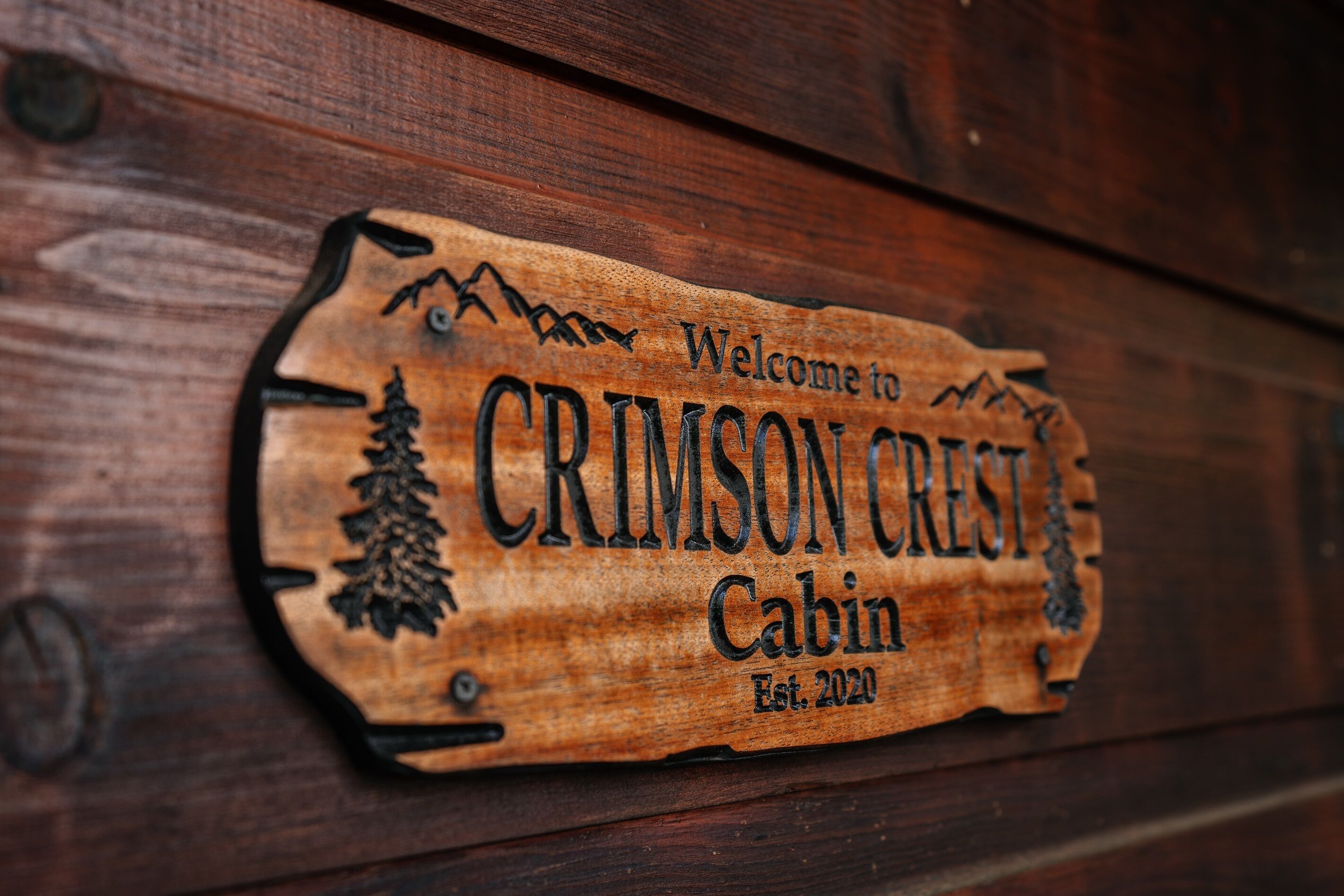 Een houten bord met de tekst 'Welcome to CRIMSON CREEST Cabin Est. 2020'.