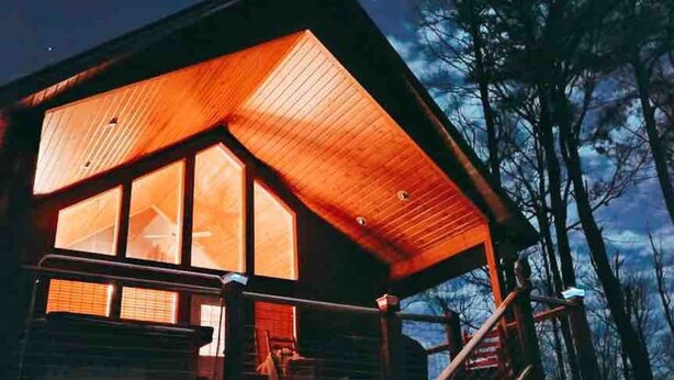 A cabin with a large window, a wooden deck, and a staircase leading to the entrance. - Hot Tub & Pool Table + Fire Pit - Secluded (Sevierville)