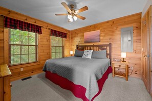 A wooden cabin bedroom with a bed, a nightstand, a ceiling fan, and a window with blinds.