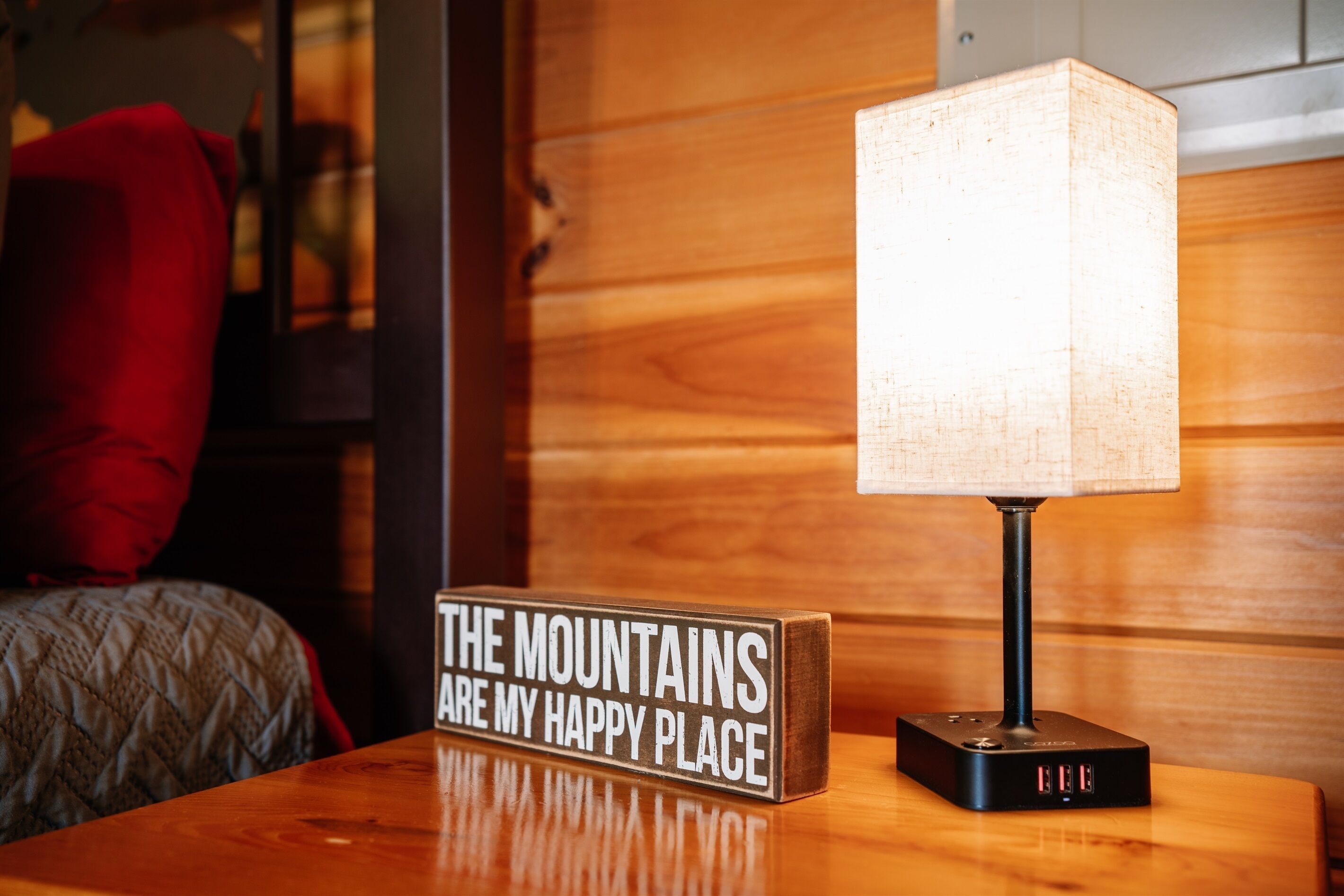 Una taula de nit de fusta amb una làmpada i un cartell que diu "THE MOUNTAINS ARE MY HAPPY PLACE".