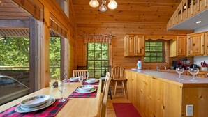 A wooden cabin interior with a dining area, kitchen, and large windows. - Hot Tub & Pool Table + Fire Pit - Secluded (Sevierville)