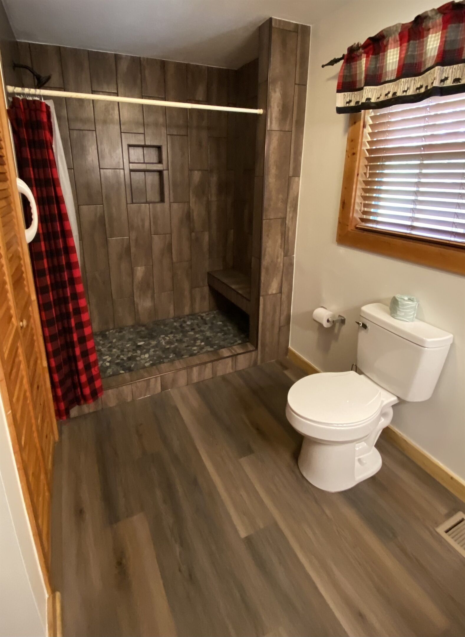 A bathroom with a shower, toilet, and a window with blinds.
