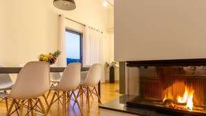 Ein modernes Wohnzimmer mit Kamin, Essbereich mit Stühlen und Blick durch ein Fenster.