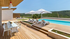 Ein moderner Poolbereich im Freien mit weißen Liegestühlen, Sonnenschirmen und einer Holzterrasse.