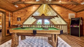 Une table de billard dans une pièce en bois, avec un plafond en pente et une vue sur l’extérieur.