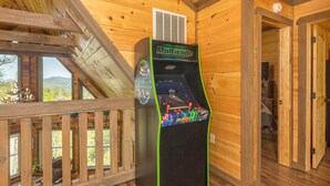 Une cabane en bois dotée d’une terrasse en bois, d’une borne d’arcade Multicade et offrant une vue sur les montagnes par les fenêtres.