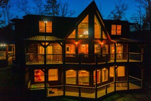 A multi-level log cabin with a balcony and large windows, surrounded by trees.